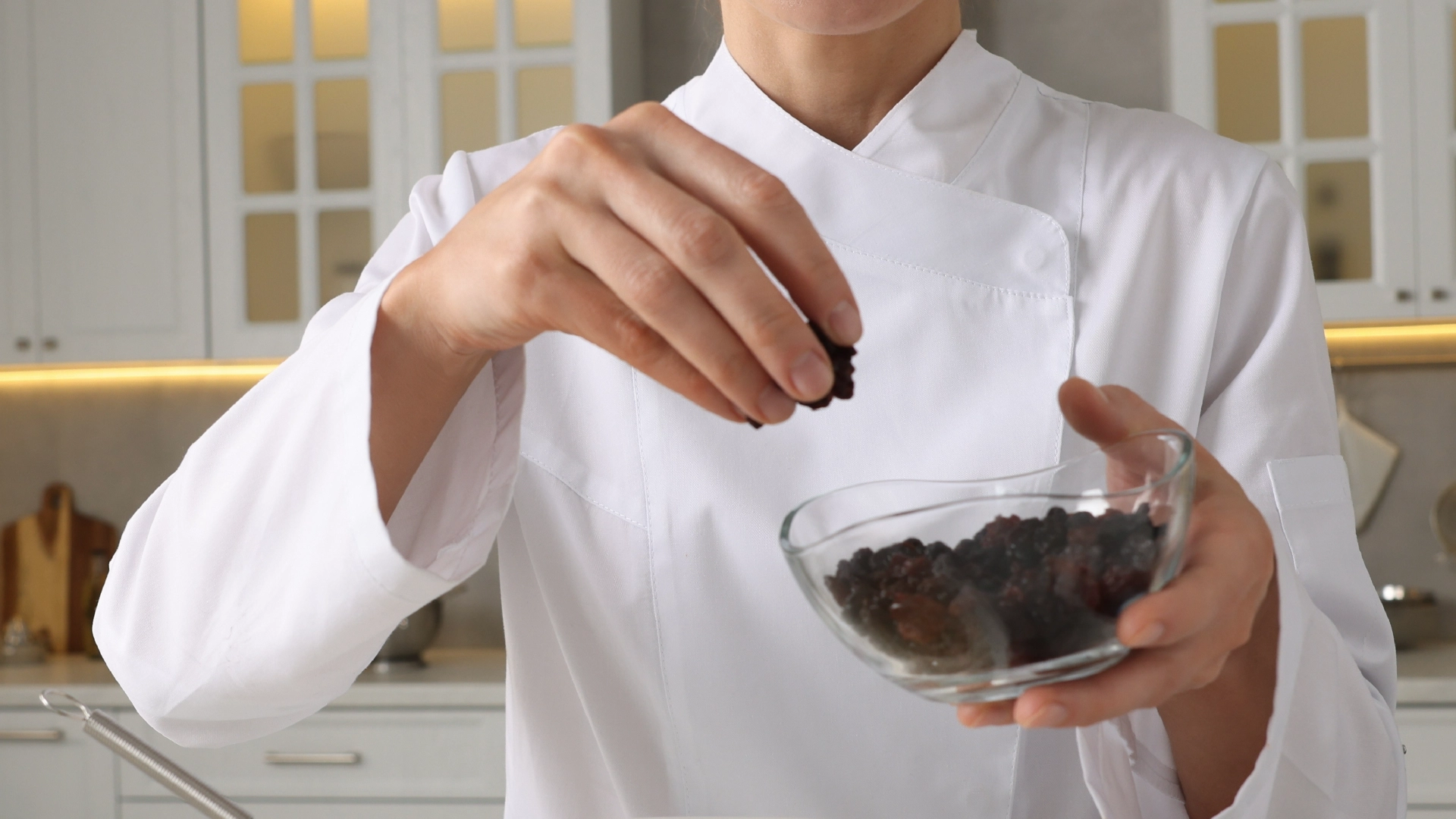 One hand holding a glass bowl of raisins while the other sprinkles them.