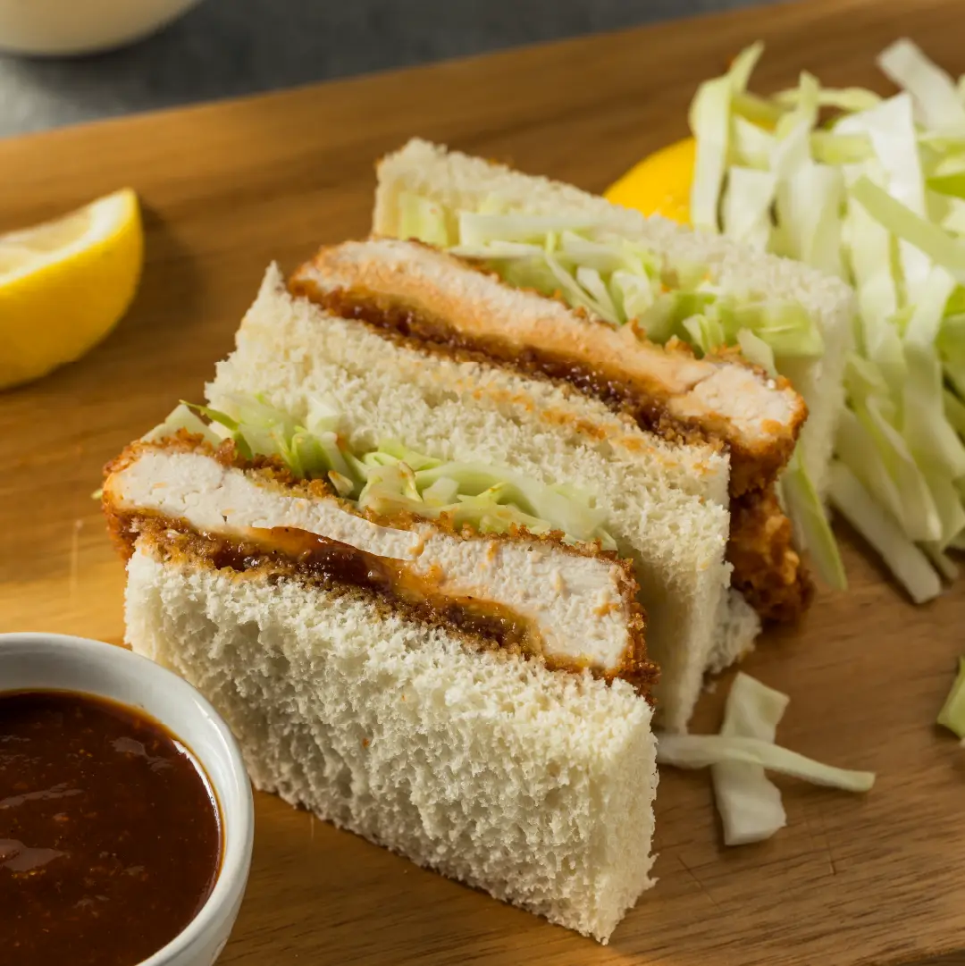 Crispy breaded chicken and shredded cabbage sandwiched between two crustless slices of white bread, cut into smaller rectangles.