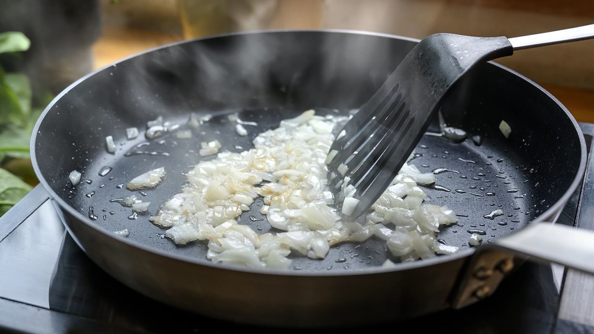 Sliced onions frying in a frying pan, being stirred with a spatula.