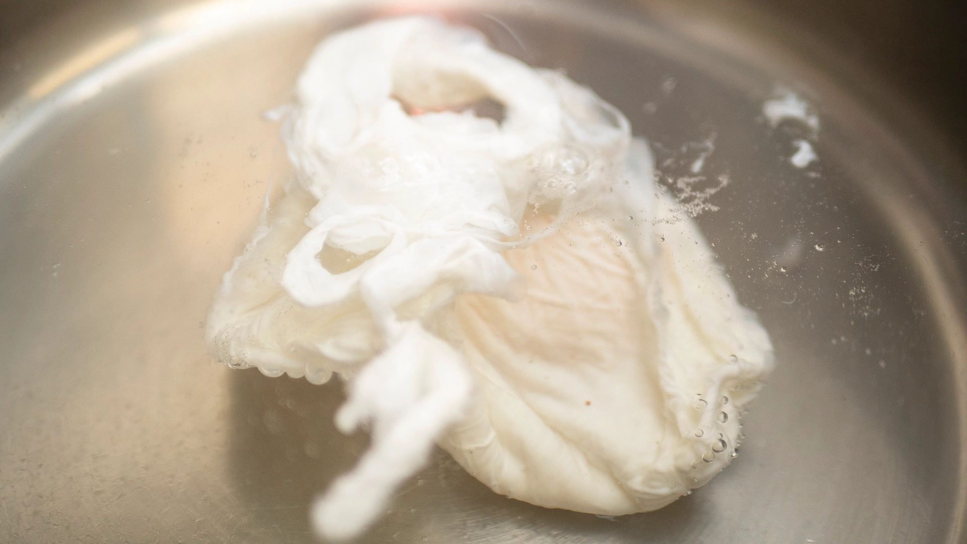 A poached egg simmering in a pot of water.