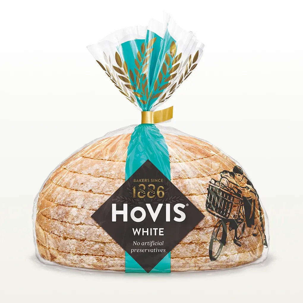 Hovis White Half Cob bread on a white backdrop with a subtle shadow, featuring packaging decorated with a light teal stripe and golden wheats.