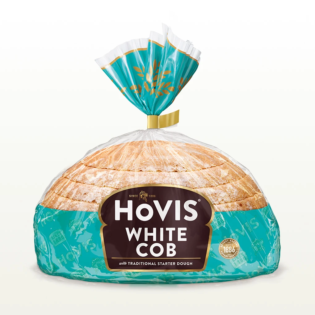 Hovis White Half Cob bread on a white backdrop with a subtle shadow, featuring packaging decorated with a light teal stripe and golden wheats.