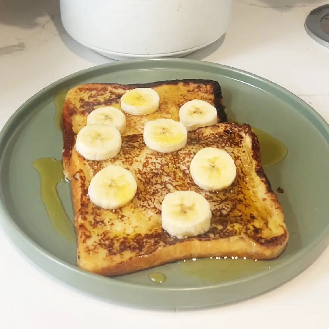 Two slices of delicious French toast rest on a green plate, with some honey and banana on top.