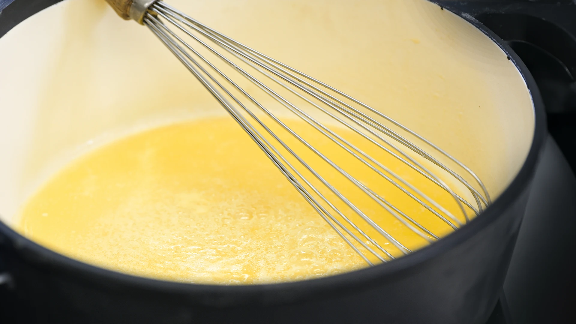 A glass bowl containing beaten eggs and a whisk.