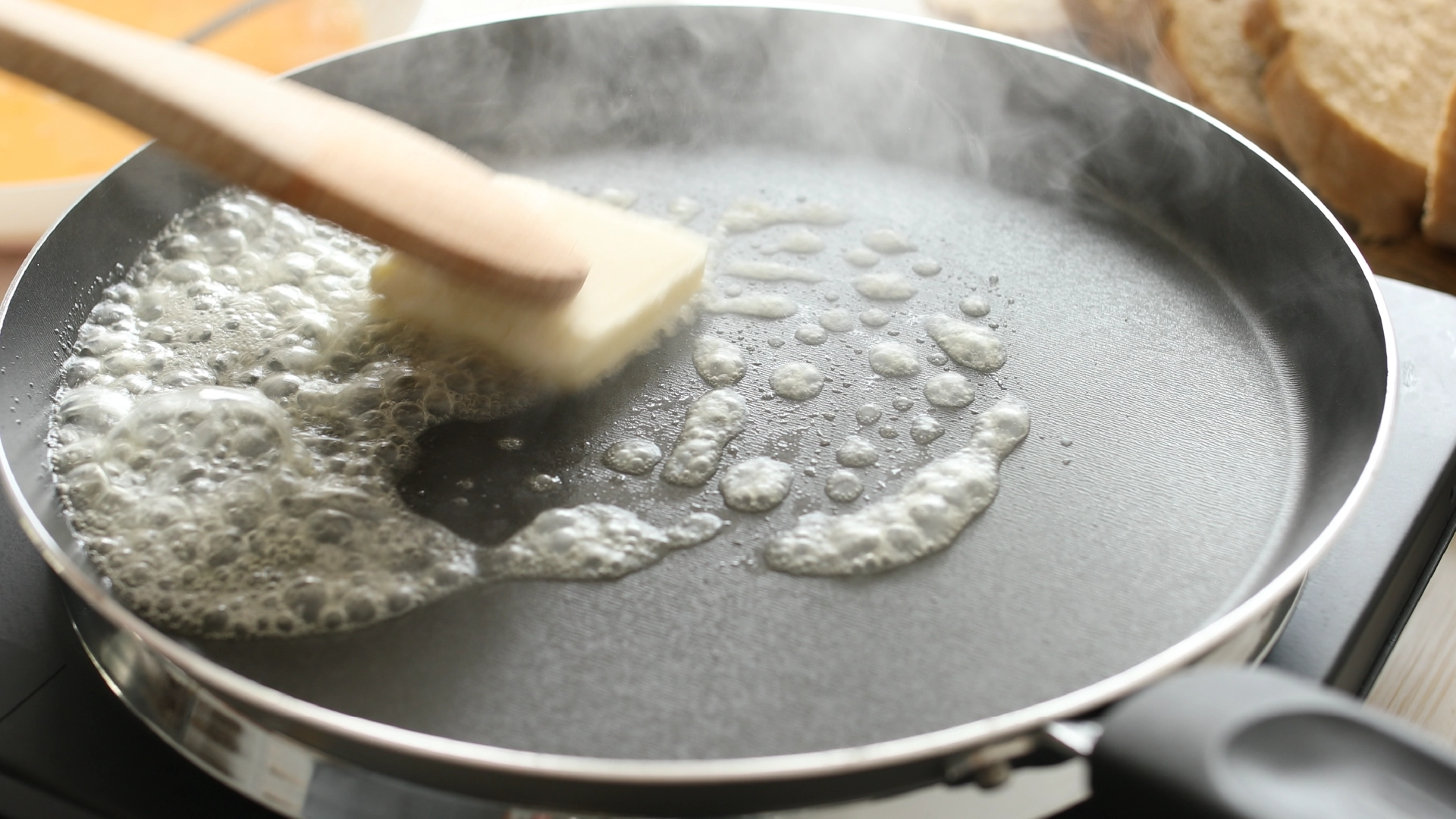 A frying pan with a small block of butter melting and steam rising from it.