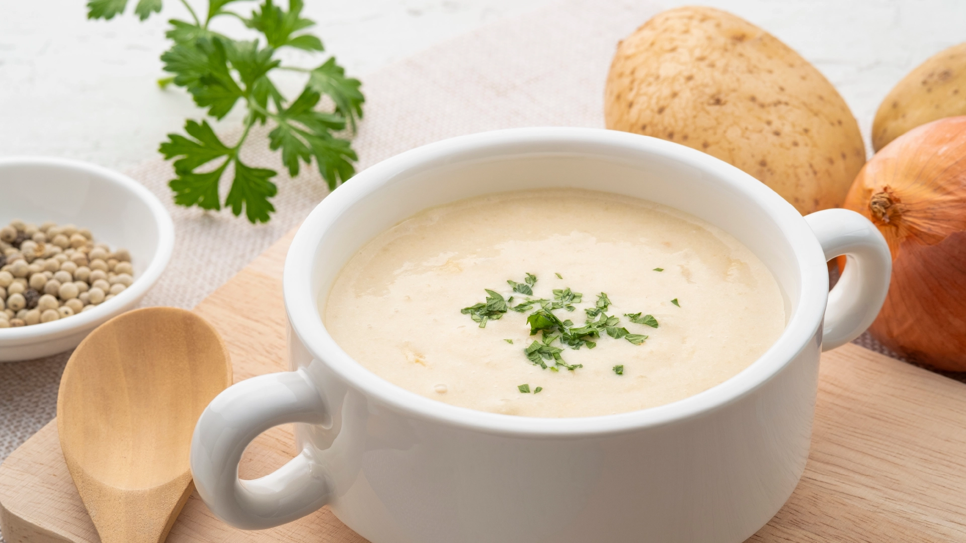 A white bowl filled with creamy beige potato soup, topped with sliced parsley.