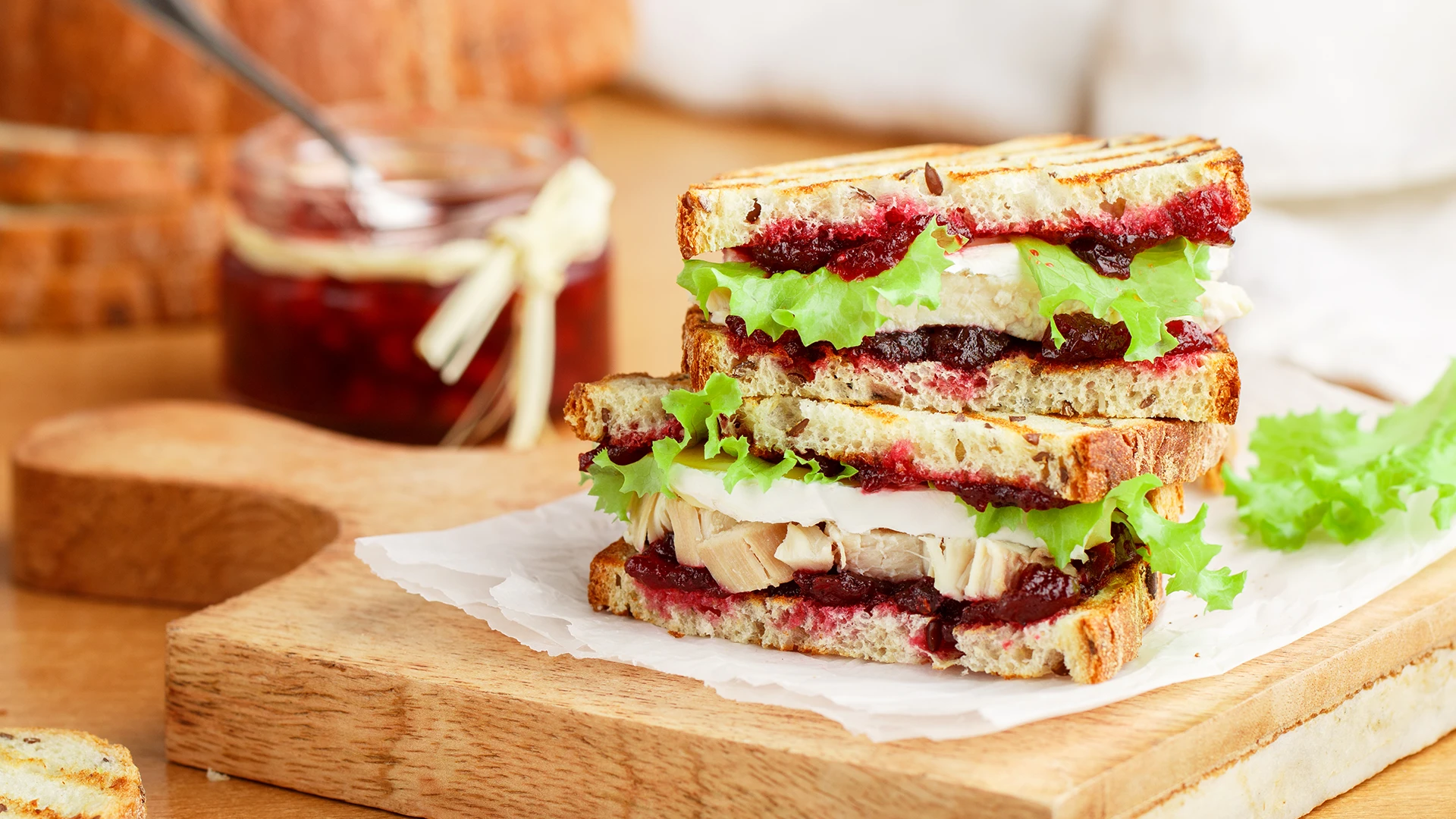 Three Hovis Seed Sensations sandwiches sliced in half all stacked in a plate, filled with cranberry sauce, pieces of turkey and brie cheese.