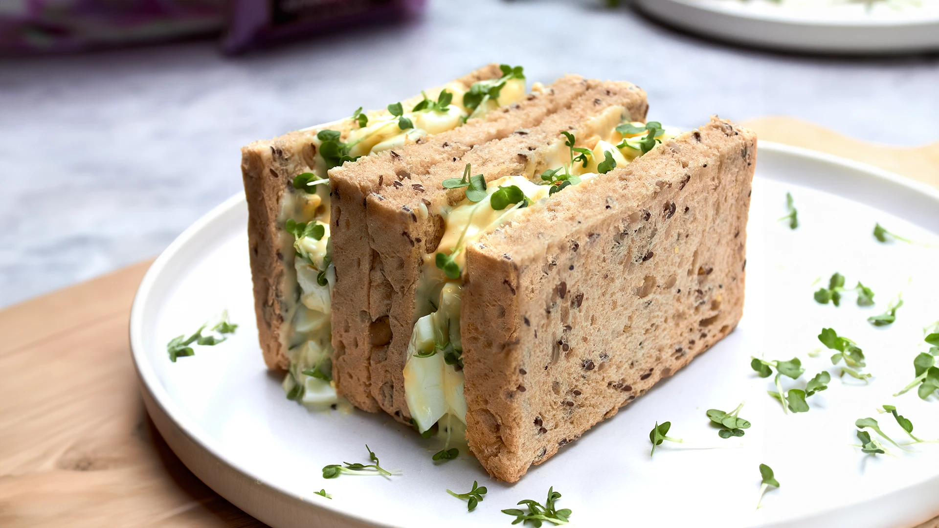 A plate with four triangular sandwiches made of brown bread, filled with egg mayonnaise and cress.