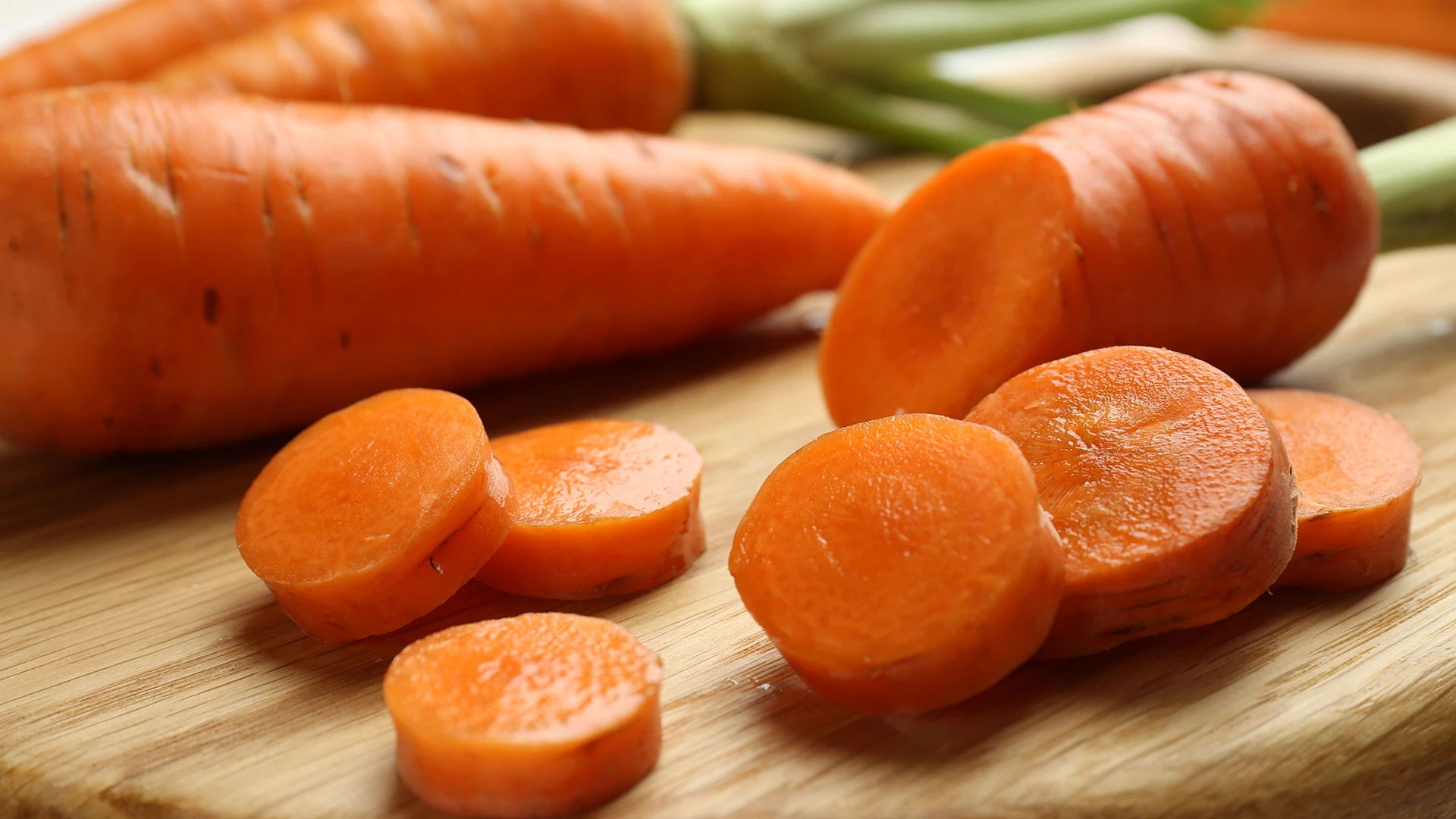 A hand transferring round carrot slices from a plate into a large pot.