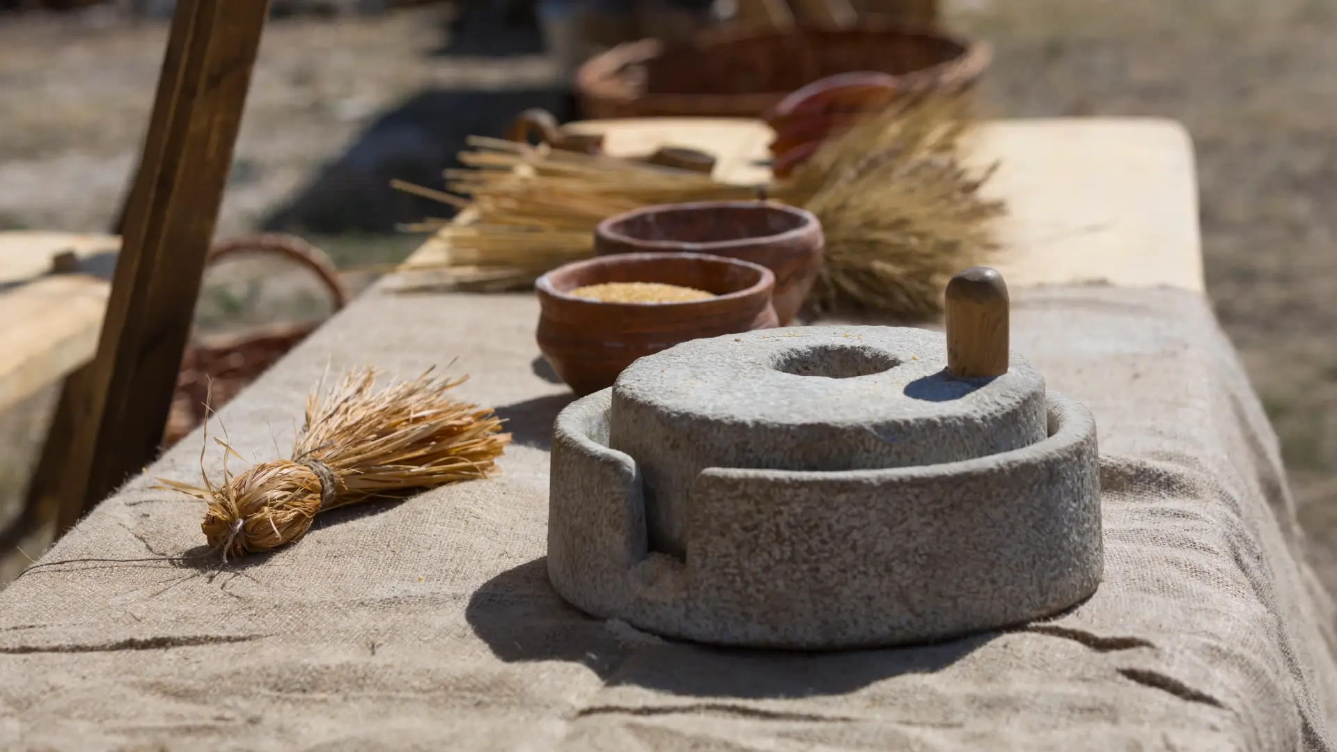 A table with an ancient stone hand mill and some wheat on the side.