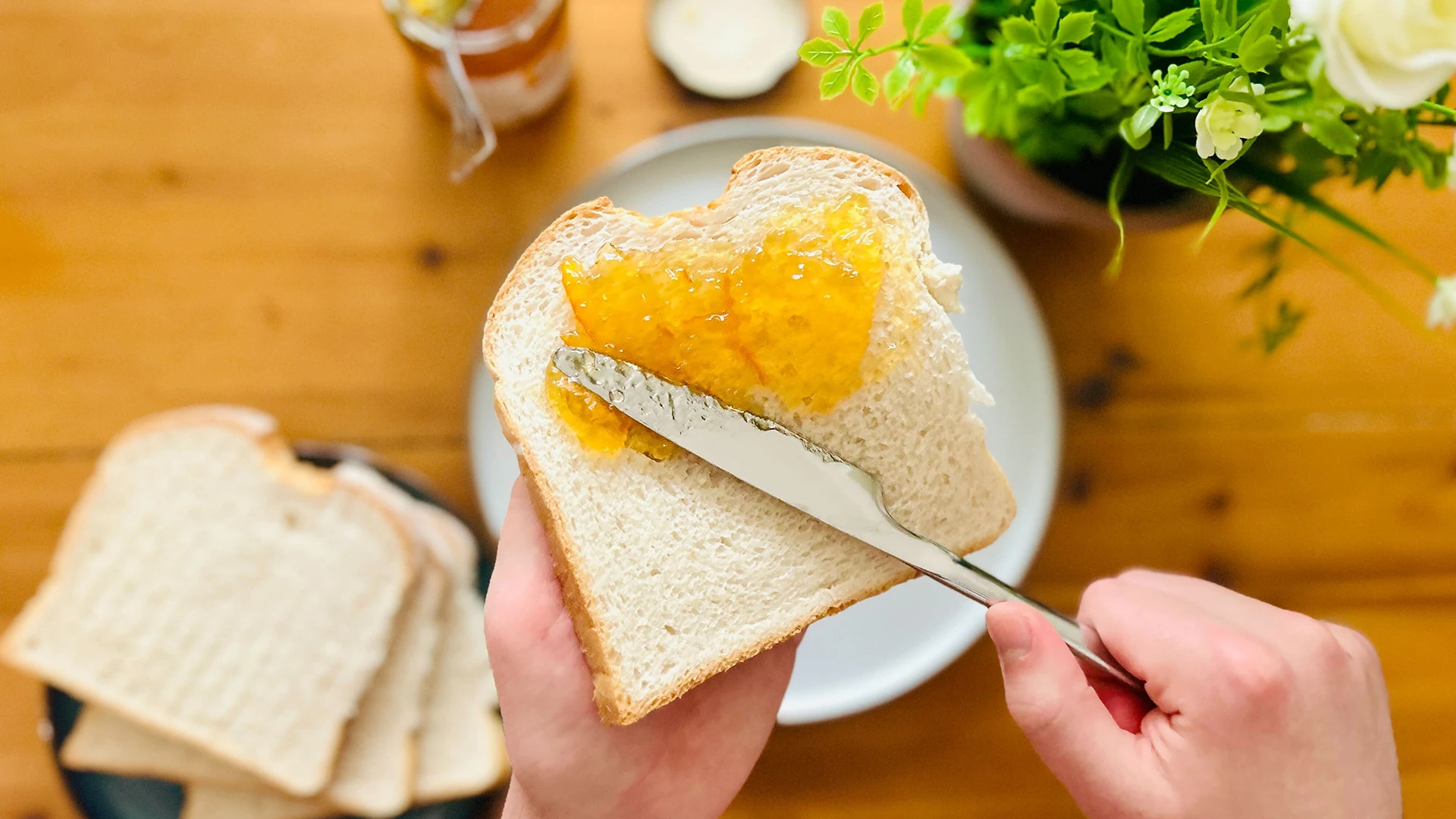 Someone is holding a slice of bread and spreading orange marmalade across the slice with a knife.