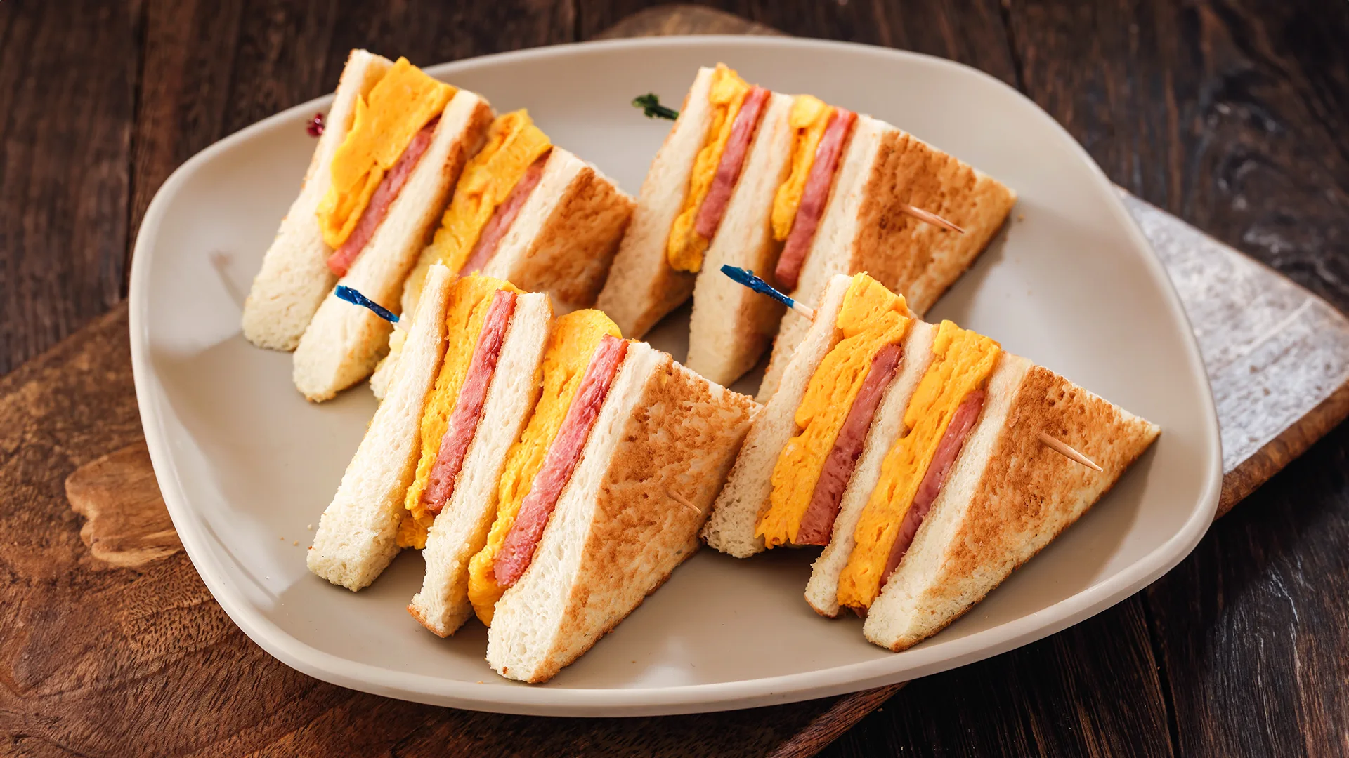 Plate of Hong Kong style scrambled egg and spam sandwiches on a wooden table.