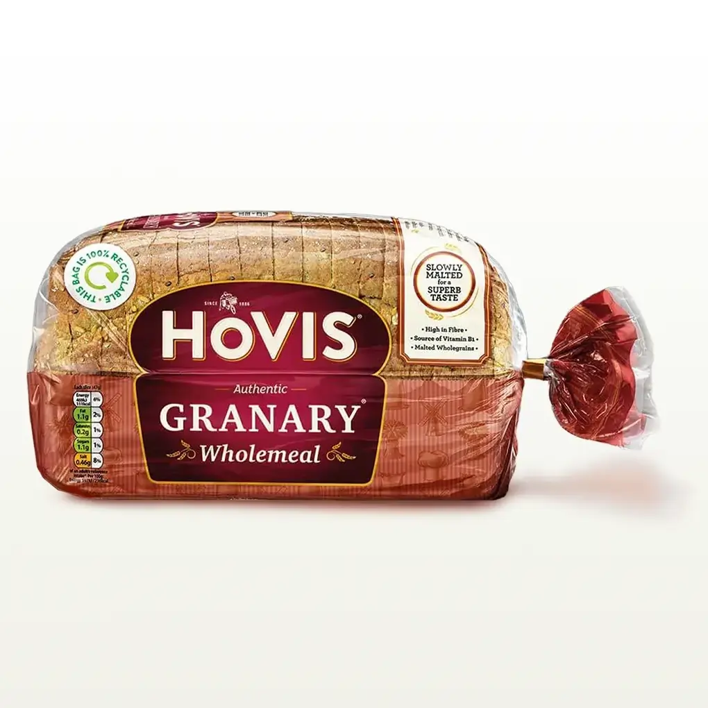 Hovis Granary Wholemeal bread on a white backdrop with a subtle shadow. The packaging is half transparent and half red, decorated with images of mills, flour and wheat.