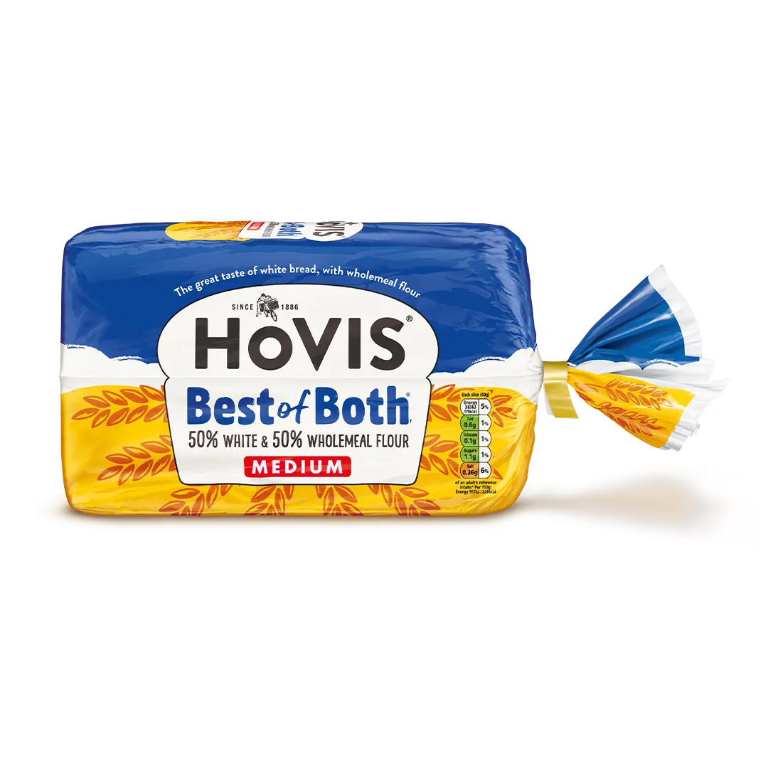 Hovis Best of Both Medium Sliced bread with a subtle shadow beneath it. The packaging features an outdoor scene with blue skies and some clouds, while the iconic Hovis loaf outline is overlaid on top of yellow wheat.