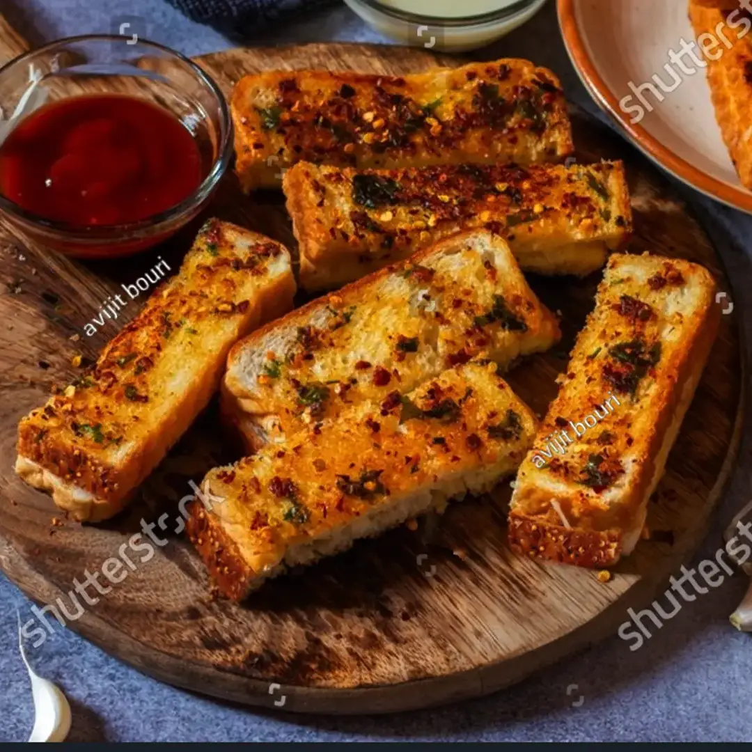 Hovis Seed Sensations Original bread, sliced in half and placed on a wooden chopping board. The slices are golden brown, topped with melted cheese and a sprinkle of thinly sliced herbs. On the side, a small bowl of ketchup and a few garlic cloves.