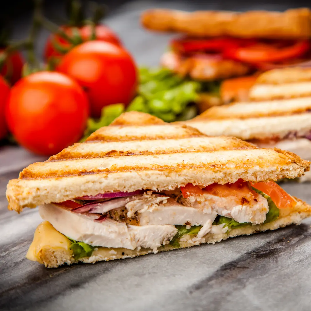 Two halves of a toasted sandwich filled with chicken, tomato, and salad leaves.