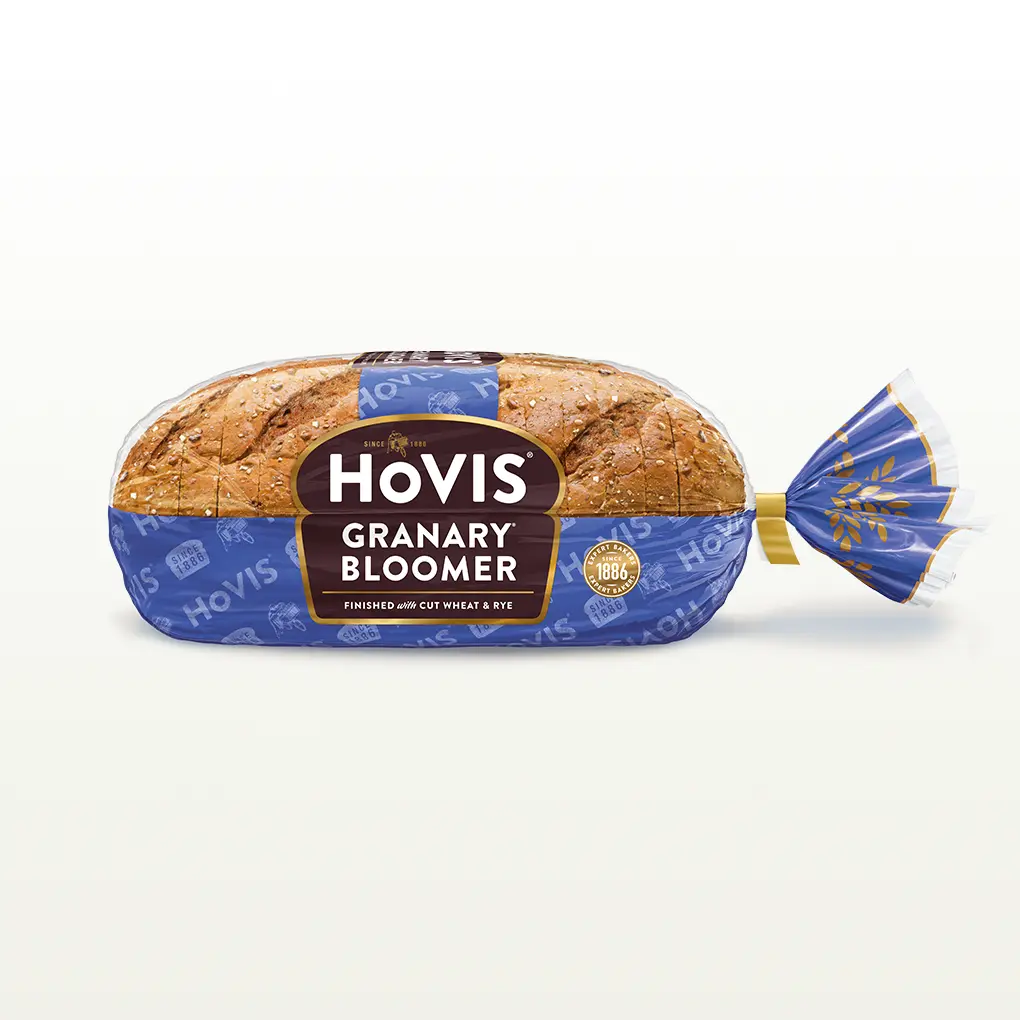 Hovis Granary Bloomer bread on a white backdrop with a subtle shadow. The packaging is half transparent and half dark blue, decorated with golden wheats.