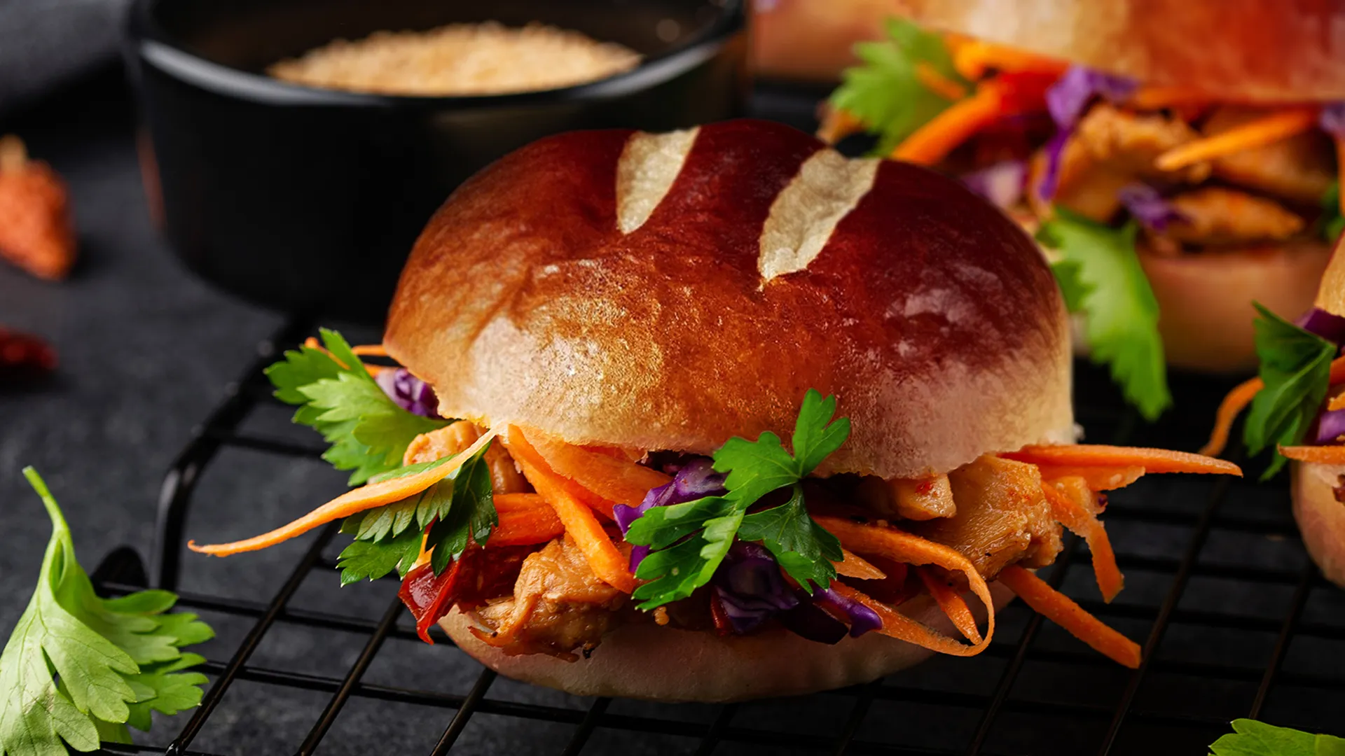 Close up of a Char Siu Banh Mi (Chinese BBQ Pork Sandwich Bun) in soft Hovis® Premium Burger Buns with coriander and some other filled buns in the background.