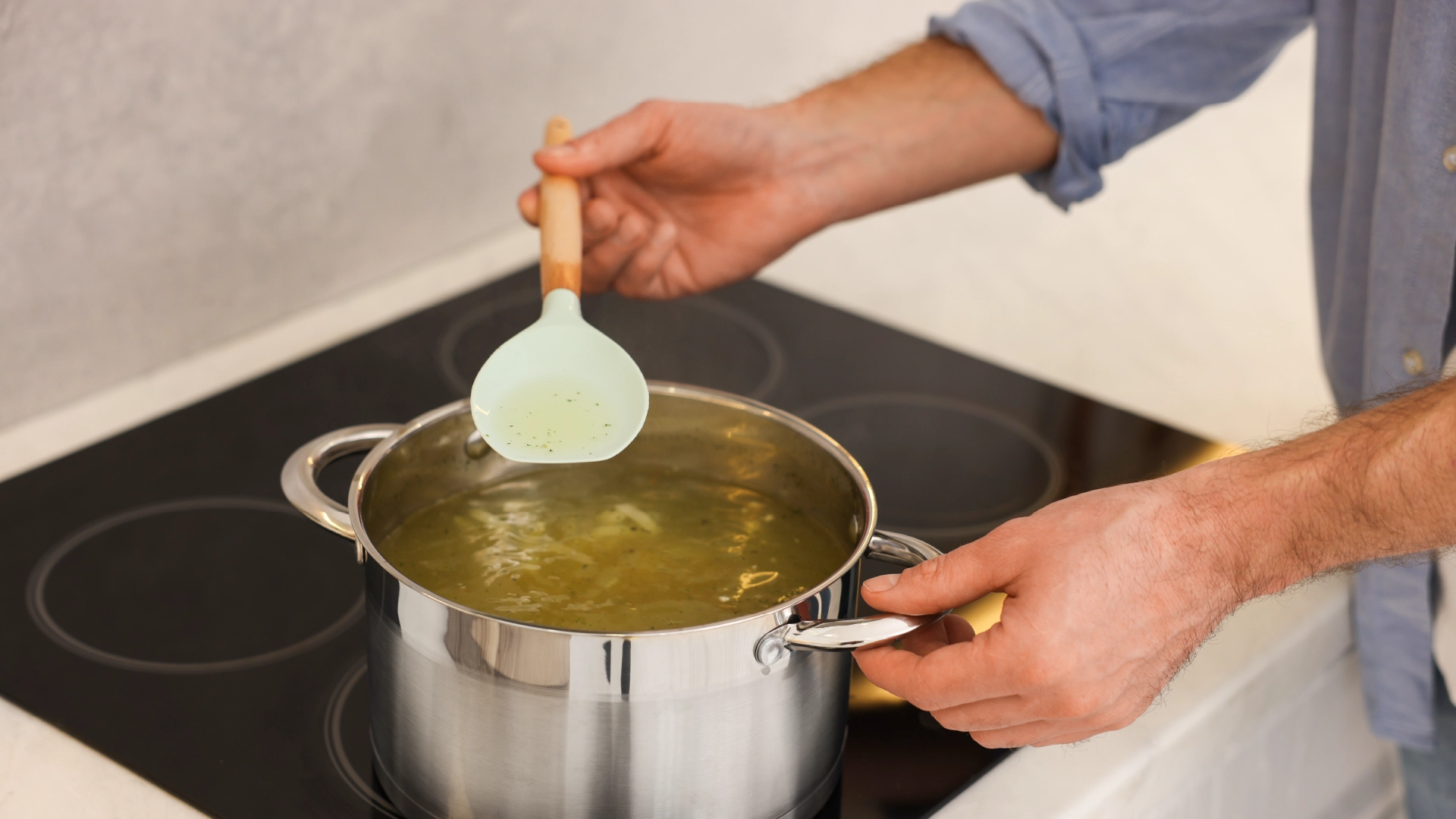 A large pot filled with simmering stock on the hob, with a hand holding a spoon.