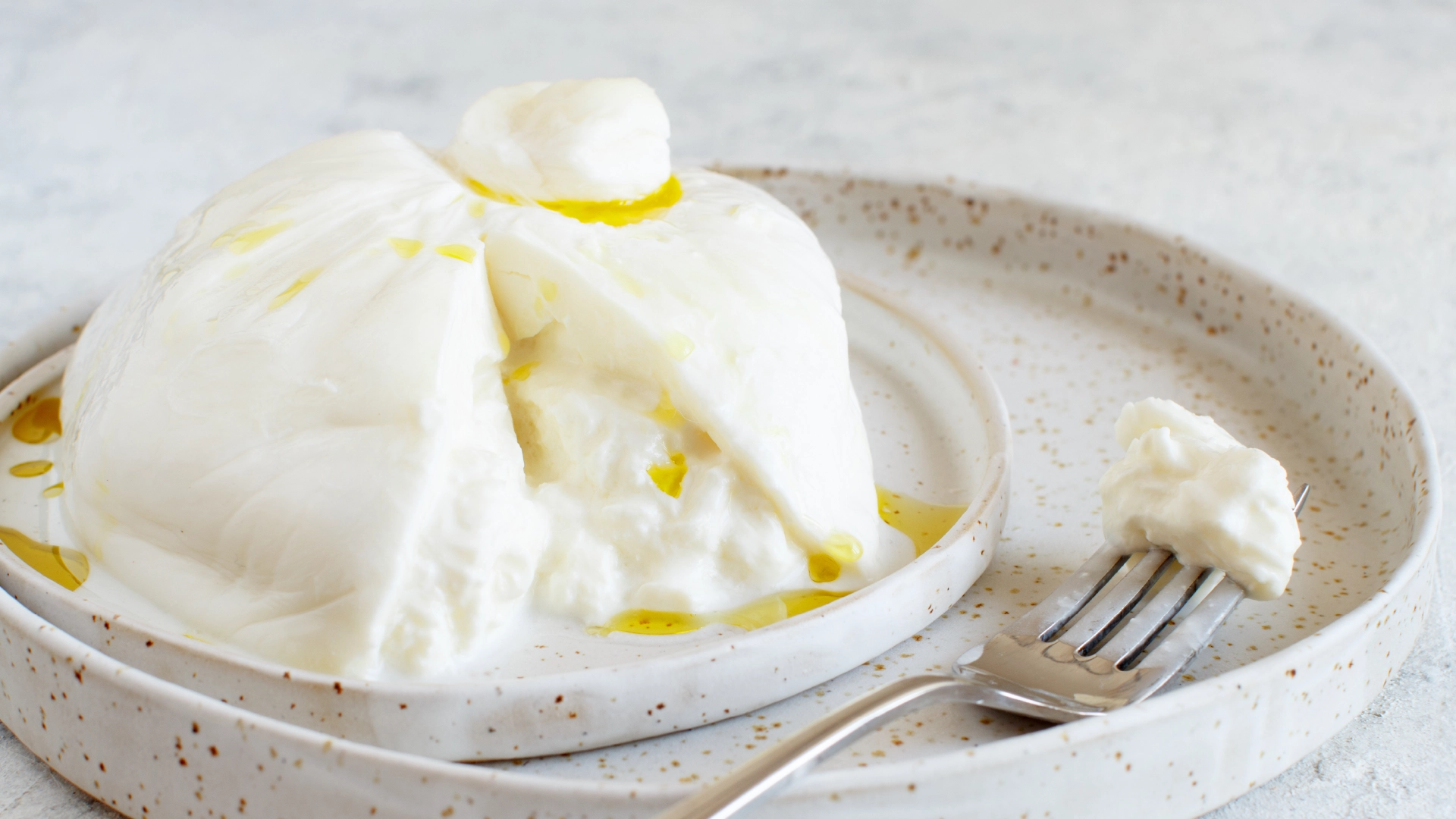 A small creamy white cheese on a plate, with a slice cut out and drizzled with olive oil on top.