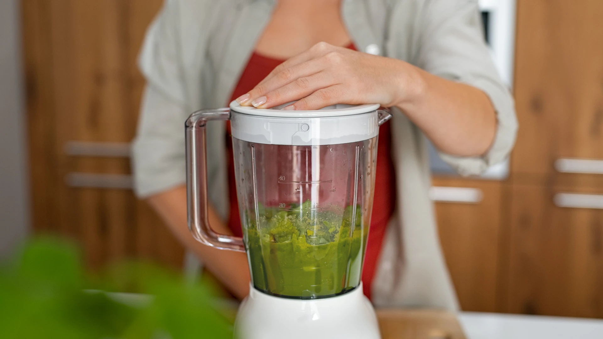 Matcha pistachio spread ingredients being blended in white food processor by a woman in a red top.