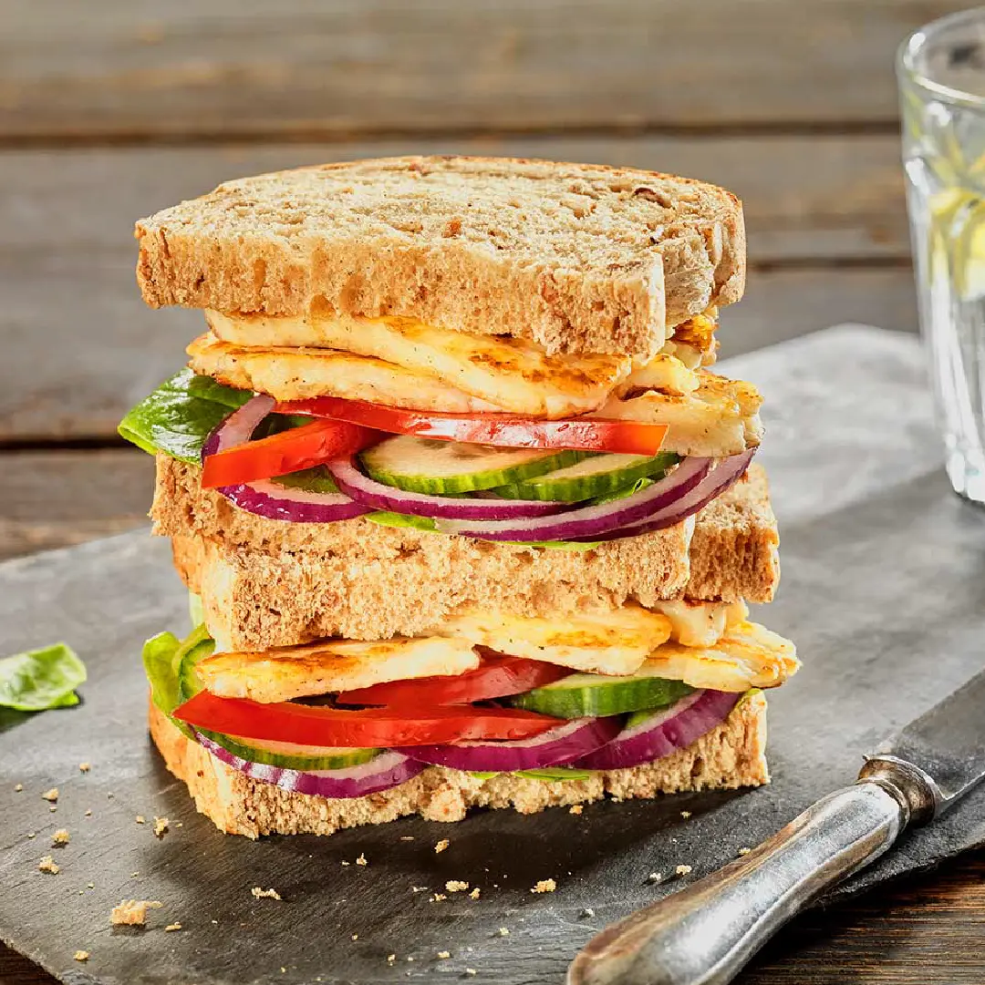 Two Hovis Granary 400g sandwiches stacked, filled with slices of red onion, cucumber, red pepper, and halloumi between brown bread slices.