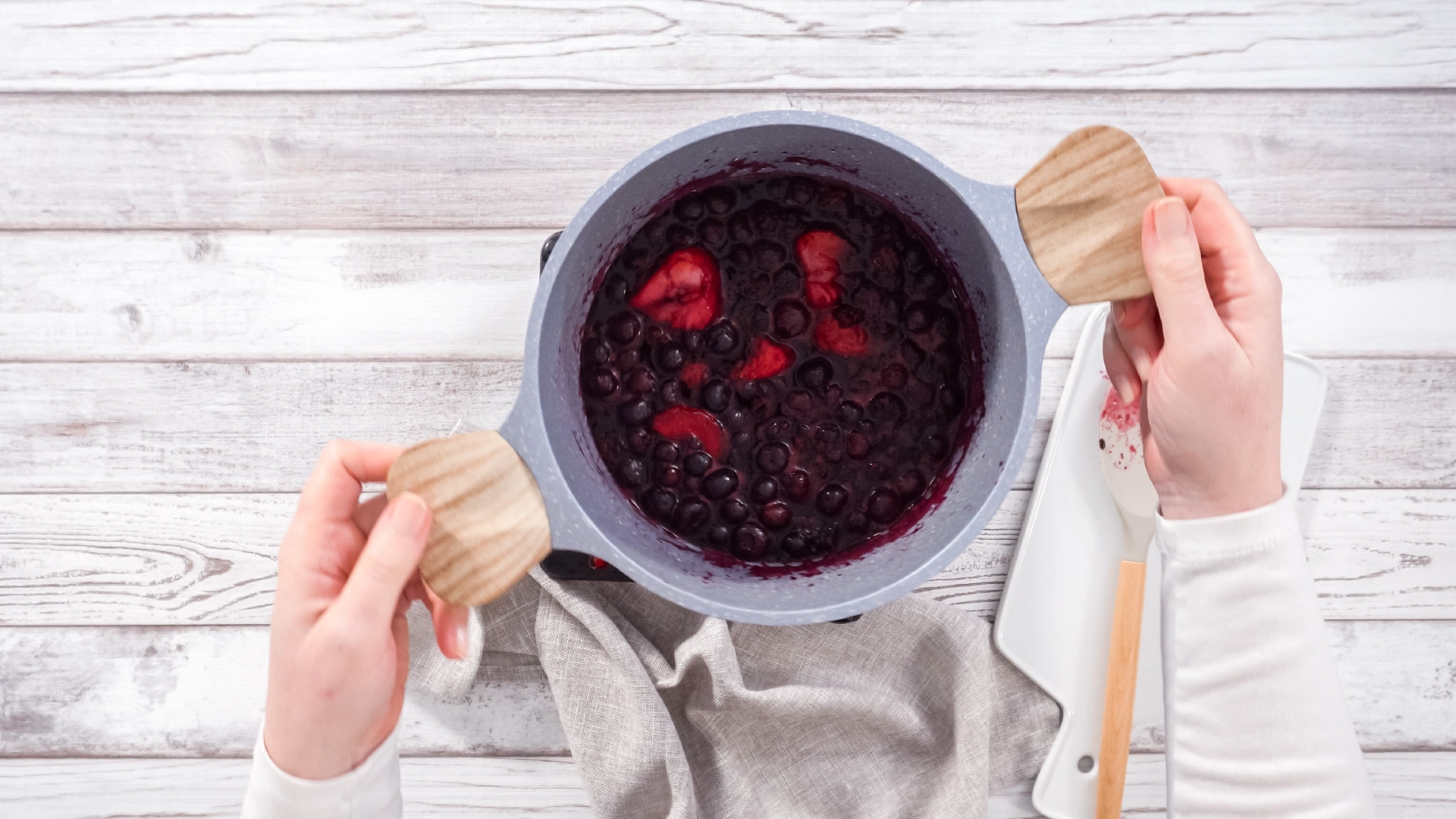 A top-down view of a person holding a medium pot filled with red berries and purple juice.