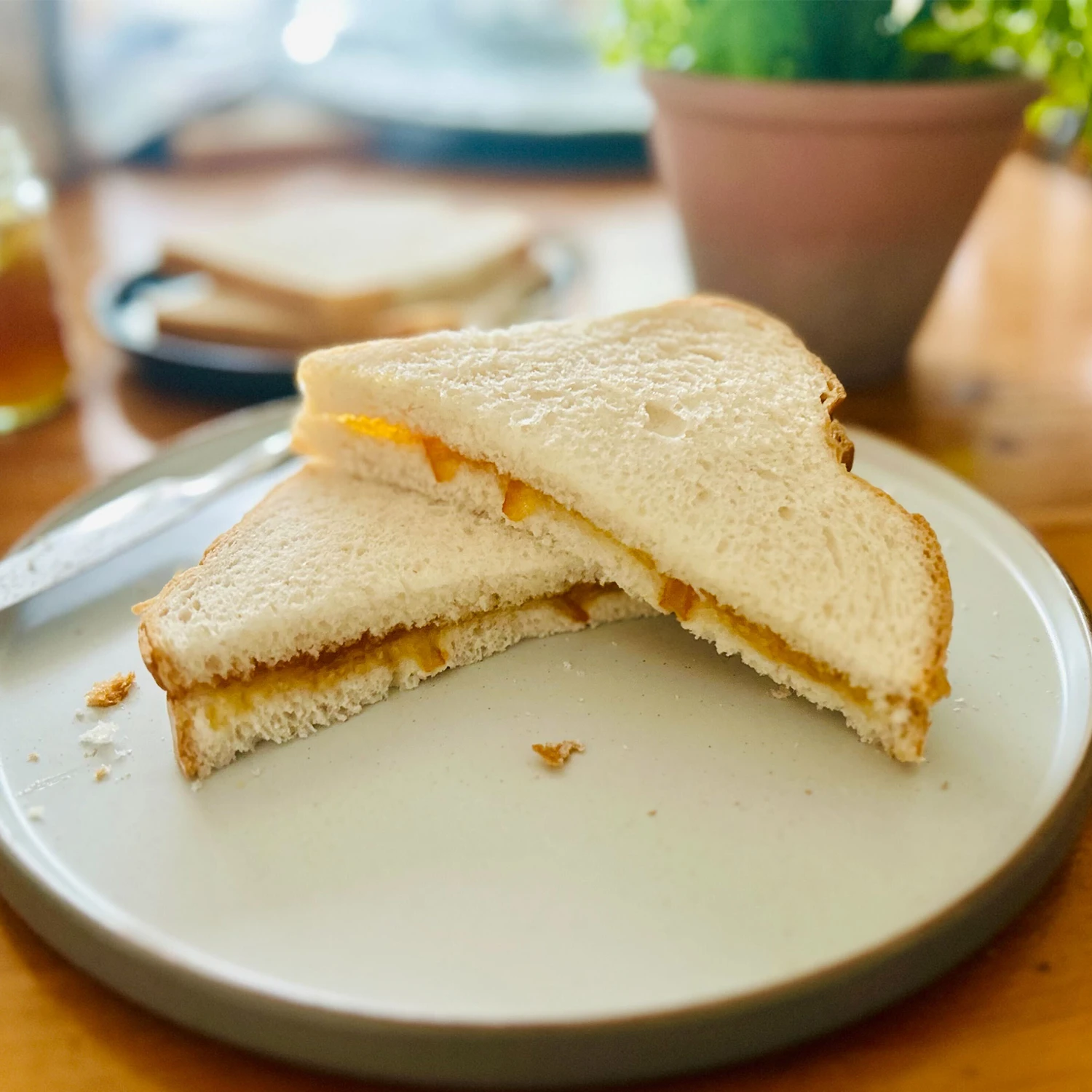 A Marmalade Sandwich cut into triangles sits on a wooden table. The sandwich is made using Hovis Farmhouse Batch.