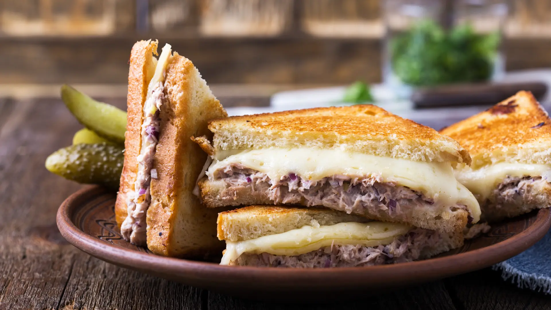 Four slices of toasted brown bread sandwiches on a plate, filled with tuna mayonnaise and molten cheese oozing between the slices.