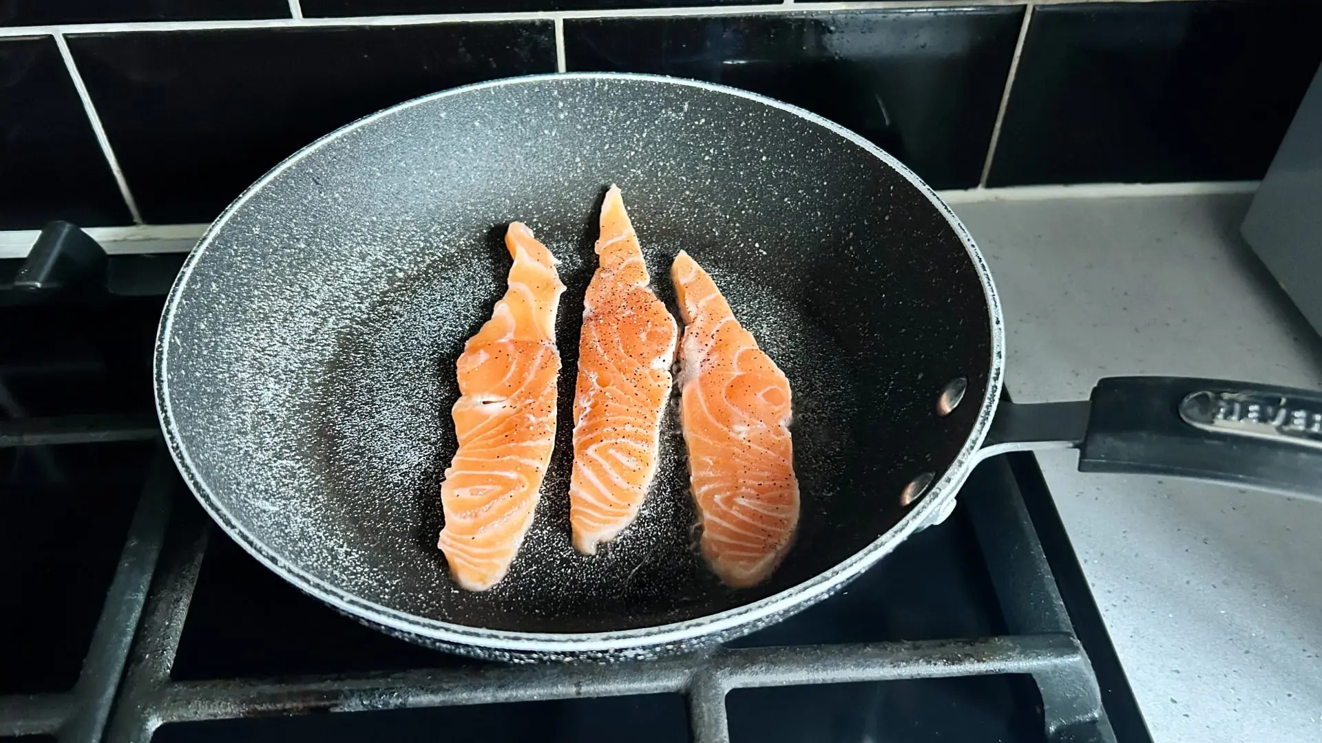 A gloved hand holds tongs to sear two pieces of salmon.