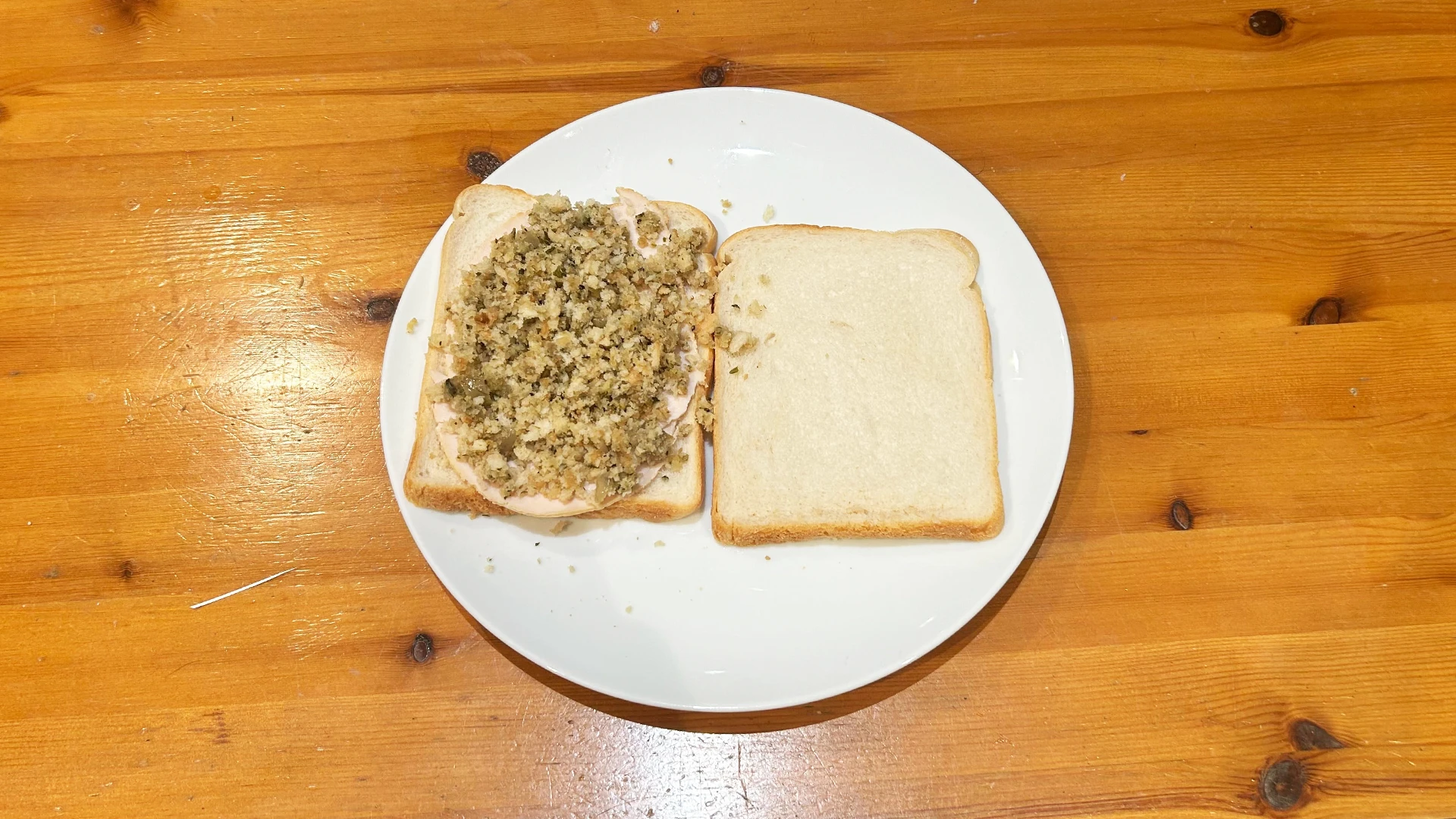 Someone added thin slices of turkey on top of a slice of Hovis Soft White Medium Sliced bread on a white plate. As well as some stuffing.