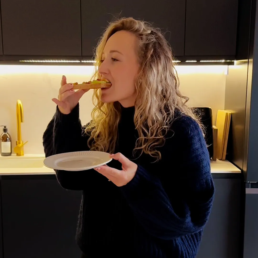 A women stands in a kitchen eating a toastie