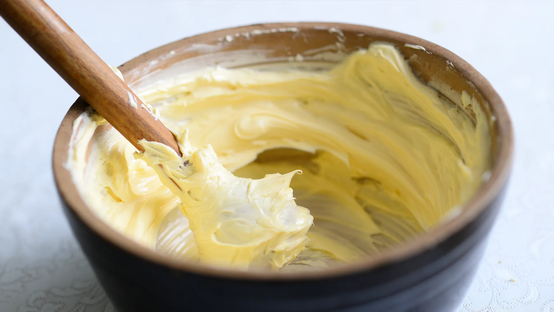 A small brown bowl filled with creamy softened butter sits on the kitchen counter. A silicone pestle with a wooden handle rests beside it.